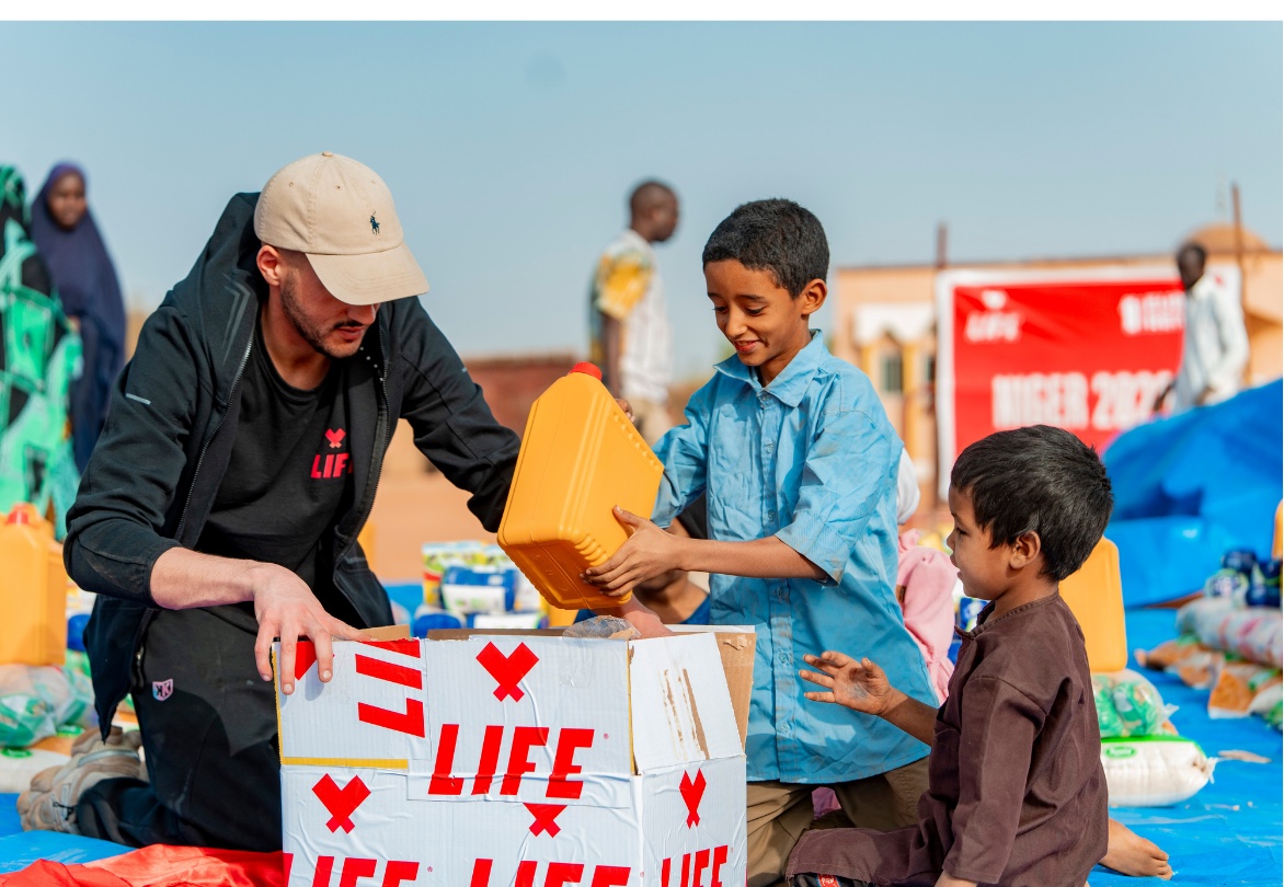 Un homme en t-shirt LIFE et un garçon rangent un bidon jaune dans un carton LIFE lors d'une distribution au Niger.